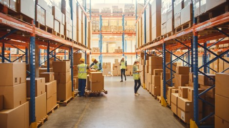 Retail Warehouse full of Shelves with Goods in Cardboard Boxes, Workers Scan and Sort Packages, Move Inventory with Pallet Trucks and Forklifts. Product Distribution Delivery Center.